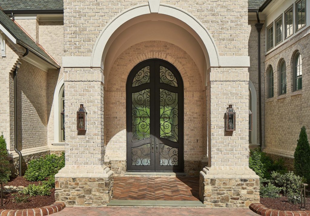 Ornate glass front door with intricate scrollwork and light brick.