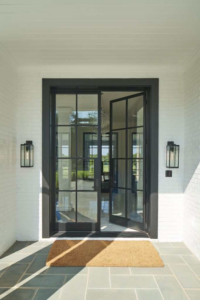 Modern front door with glass and wall sconces and doormat.