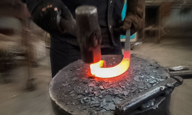 An artisan works on welding a custom wrought iron scroll.